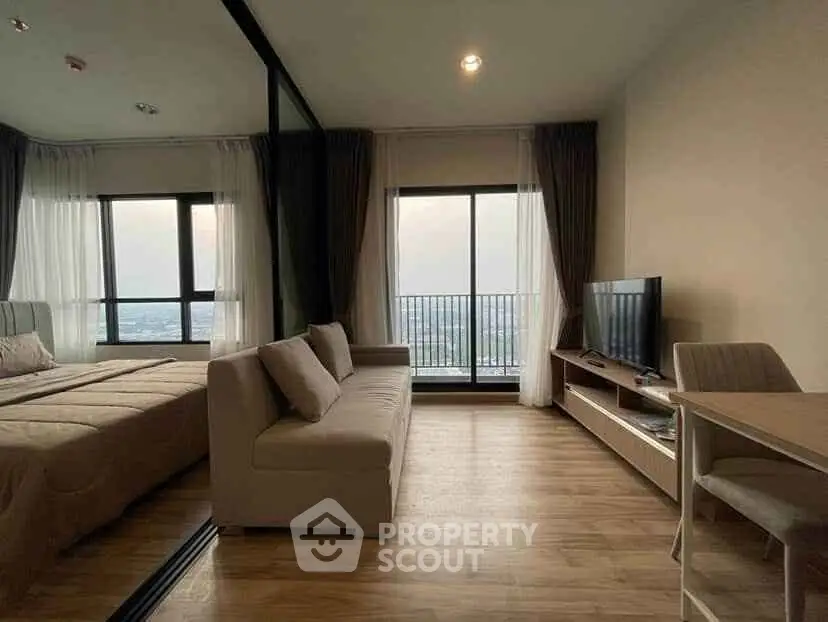 Modern living room with large windows and balcony view, featuring cozy sofa and sleek TV setup.