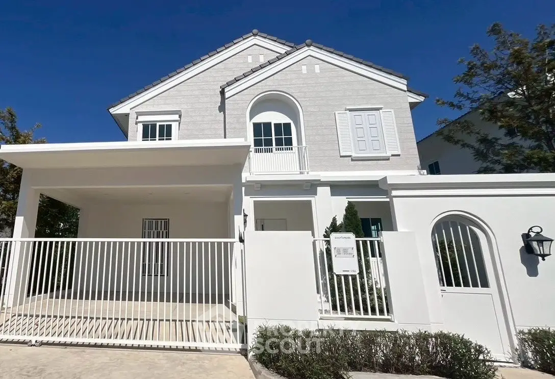 Charming white two-story house with elegant balcony and gated entrance, perfect for family living.