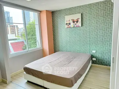 Modern bedroom with large window and stylish accent wall in urban apartment.