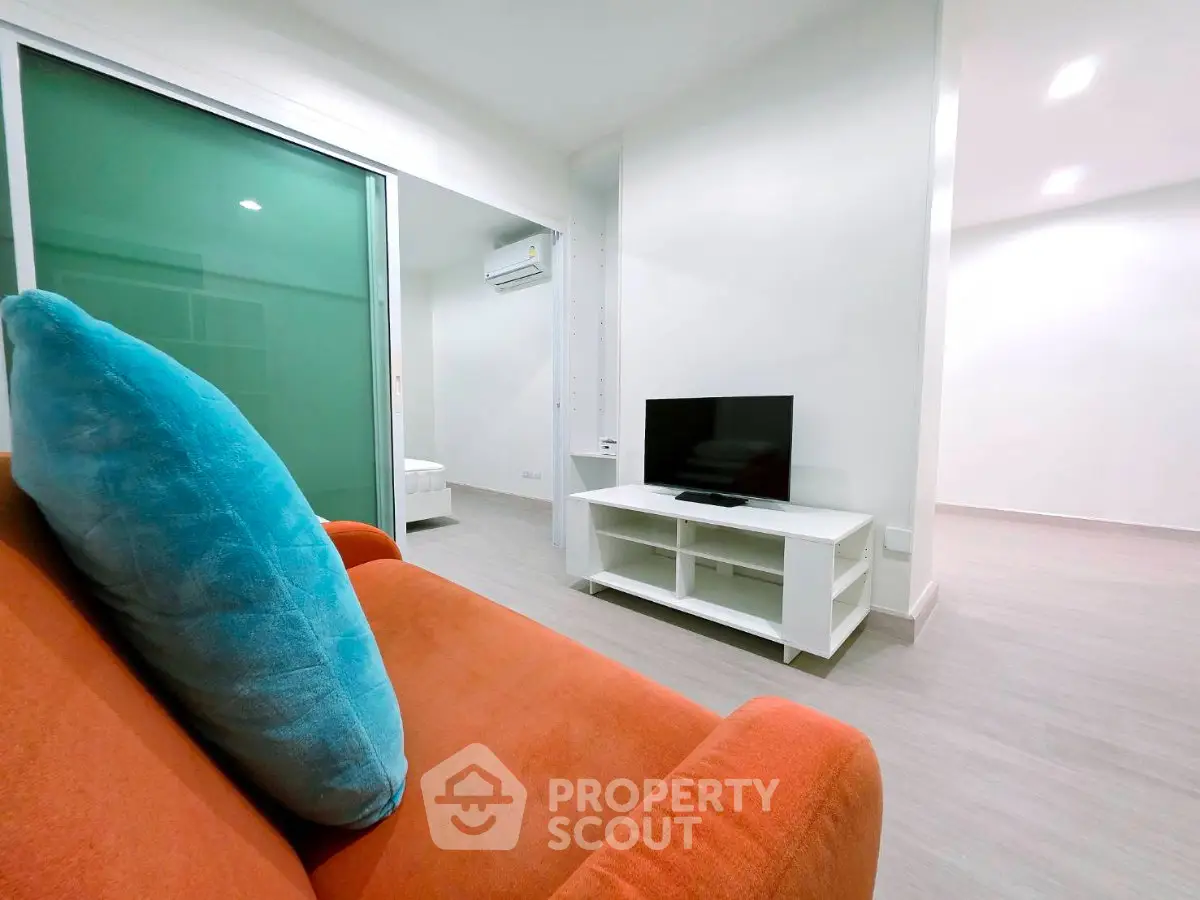 Modern living room with vibrant orange sofa and sleek TV setup in a stylish apartment.