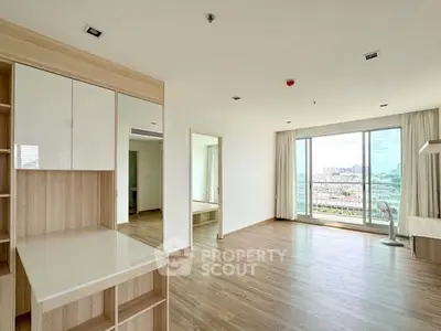 Spacious modern living room with wooden flooring and large windows offering city views.