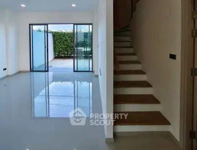 Spacious modern living room with sleek staircase and large glass doors opening to a private garden.