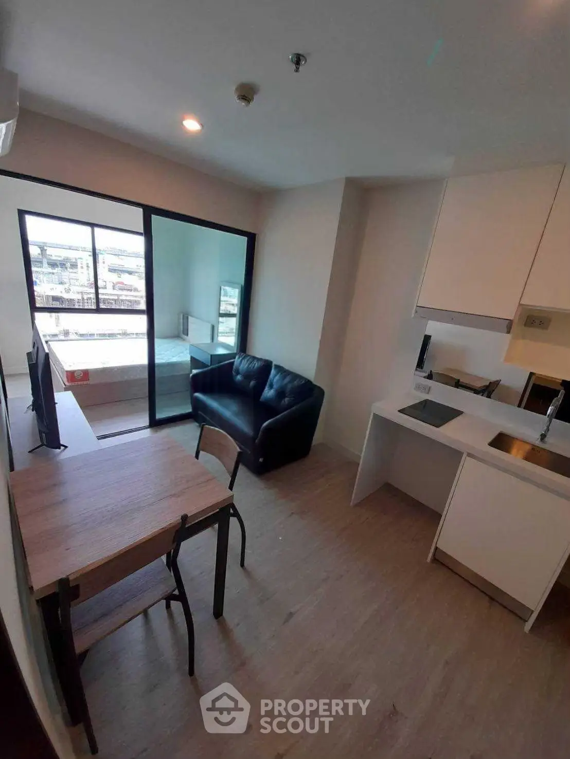 Modern open-plan living room with sleek kitchen and balcony view in urban apartment.