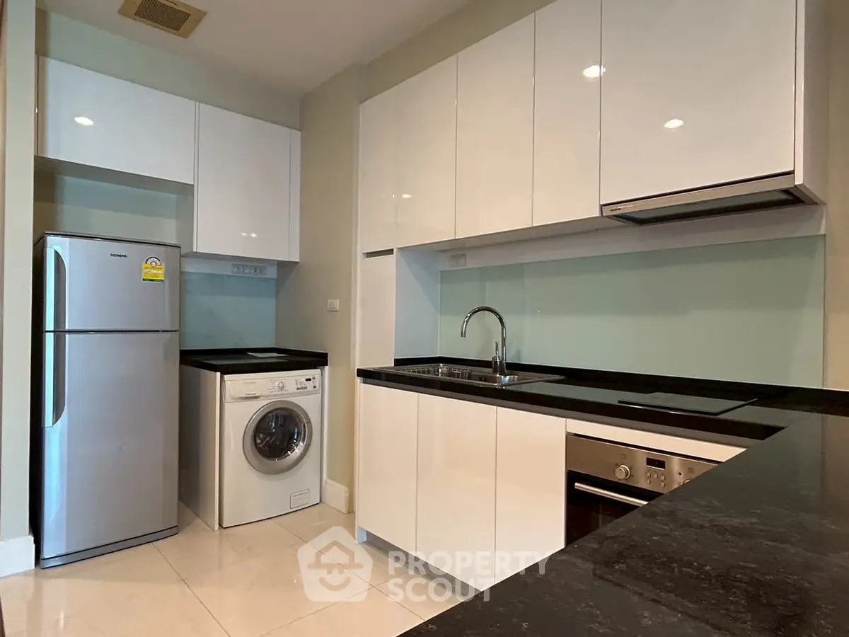 Modern kitchen with sleek cabinetry, washing machine, and built-in oven in a stylish apartment.