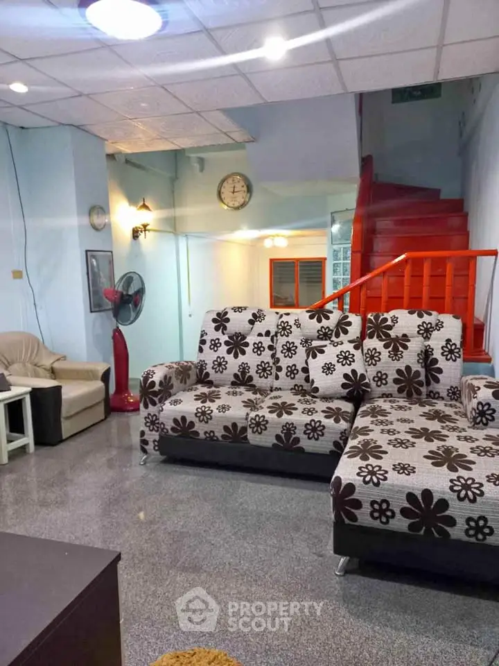 Spacious living room with floral sofas and red staircase