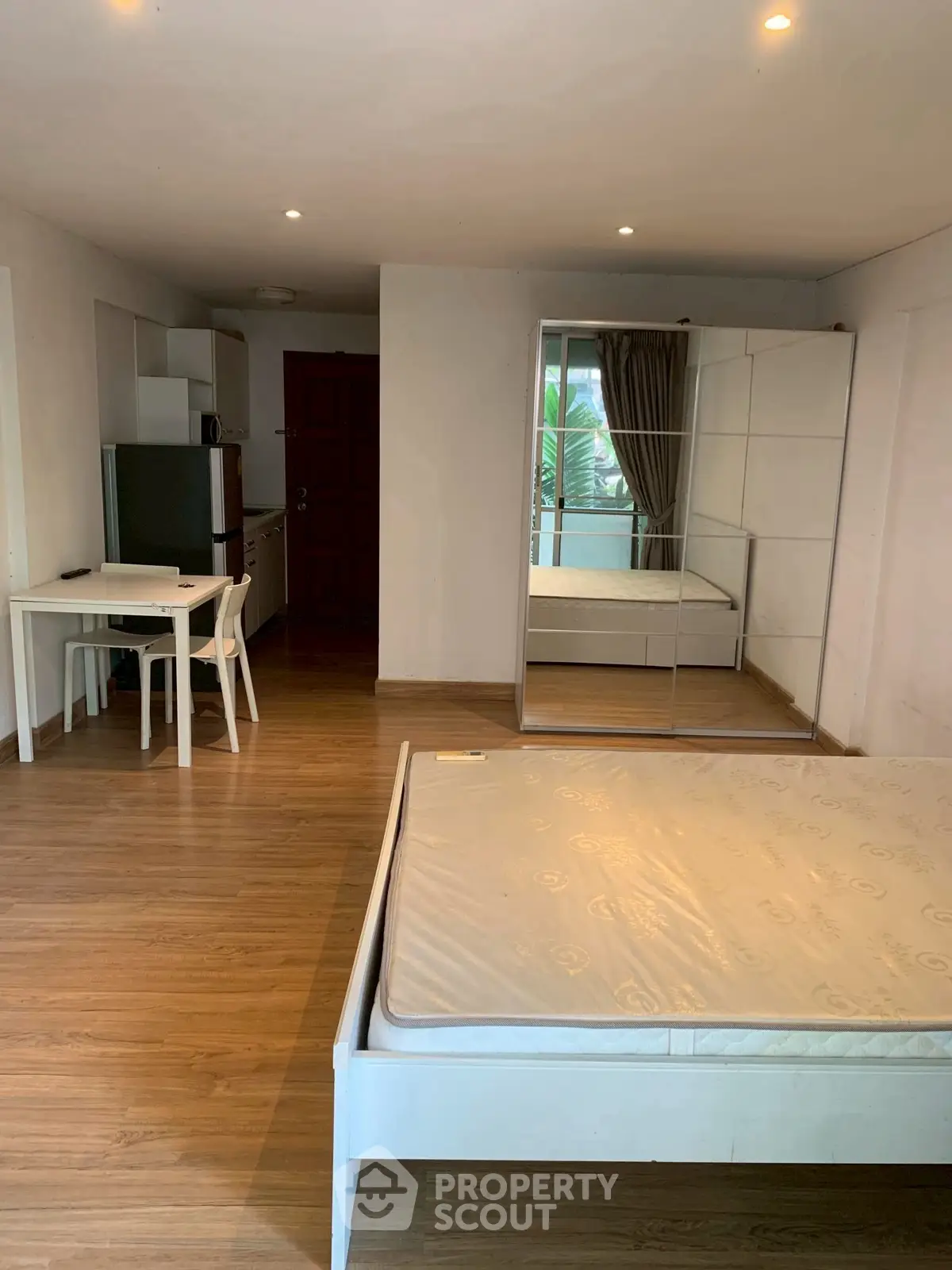 Spacious studio apartment with wooden flooring and modern furnishings, featuring a mirrored wardrobe and cozy dining area.