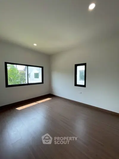 Spacious empty room with wooden flooring and large windows in modern home