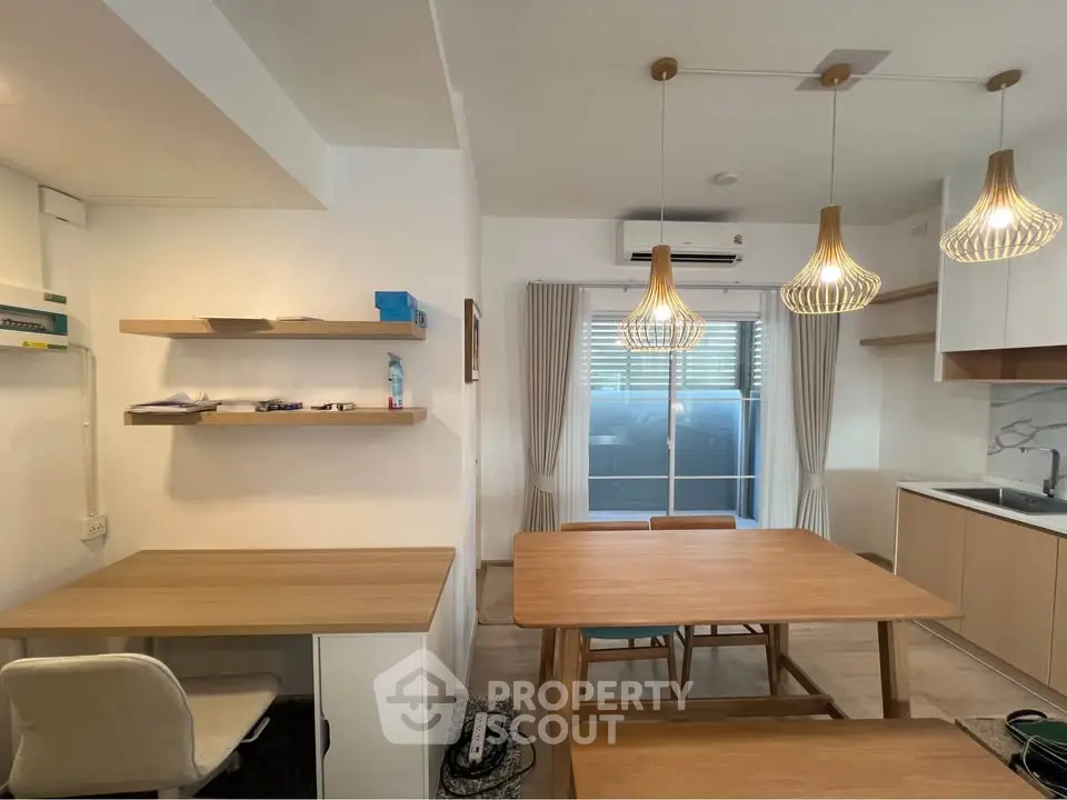 Modern open-plan living area with stylish lighting and wooden furniture, featuring a cozy workspace and kitchen.