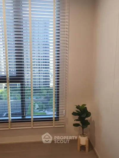 Modern apartment with large window and city view, featuring stylish blinds and a potted plant.