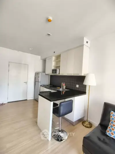 Modern kitchen with sleek black countertops and stylish bar stool in open layout apartment.