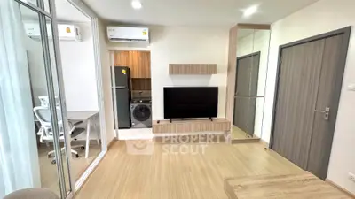 Modern living room with sleek wooden flooring and built-in TV unit, adjacent to a compact kitchen area.