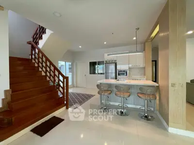 Modern open-plan kitchen with stylish bar stools and wooden staircase in a contemporary home.