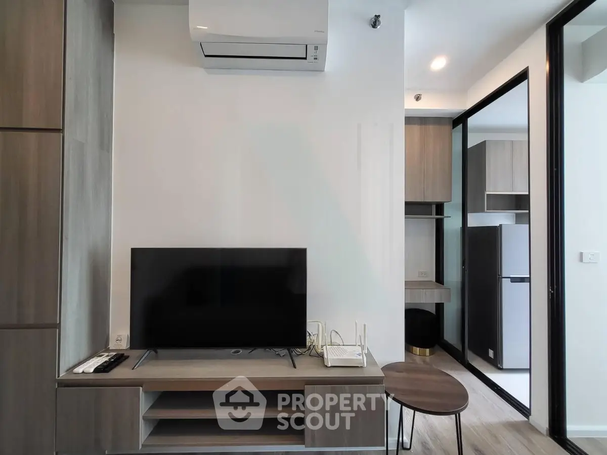 Modern living room with sleek TV setup and adjacent kitchen area in stylish apartment.