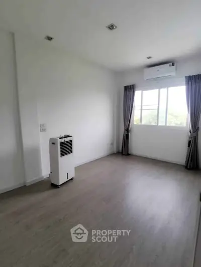 Spacious empty room with large window and air conditioning, perfect for customization.