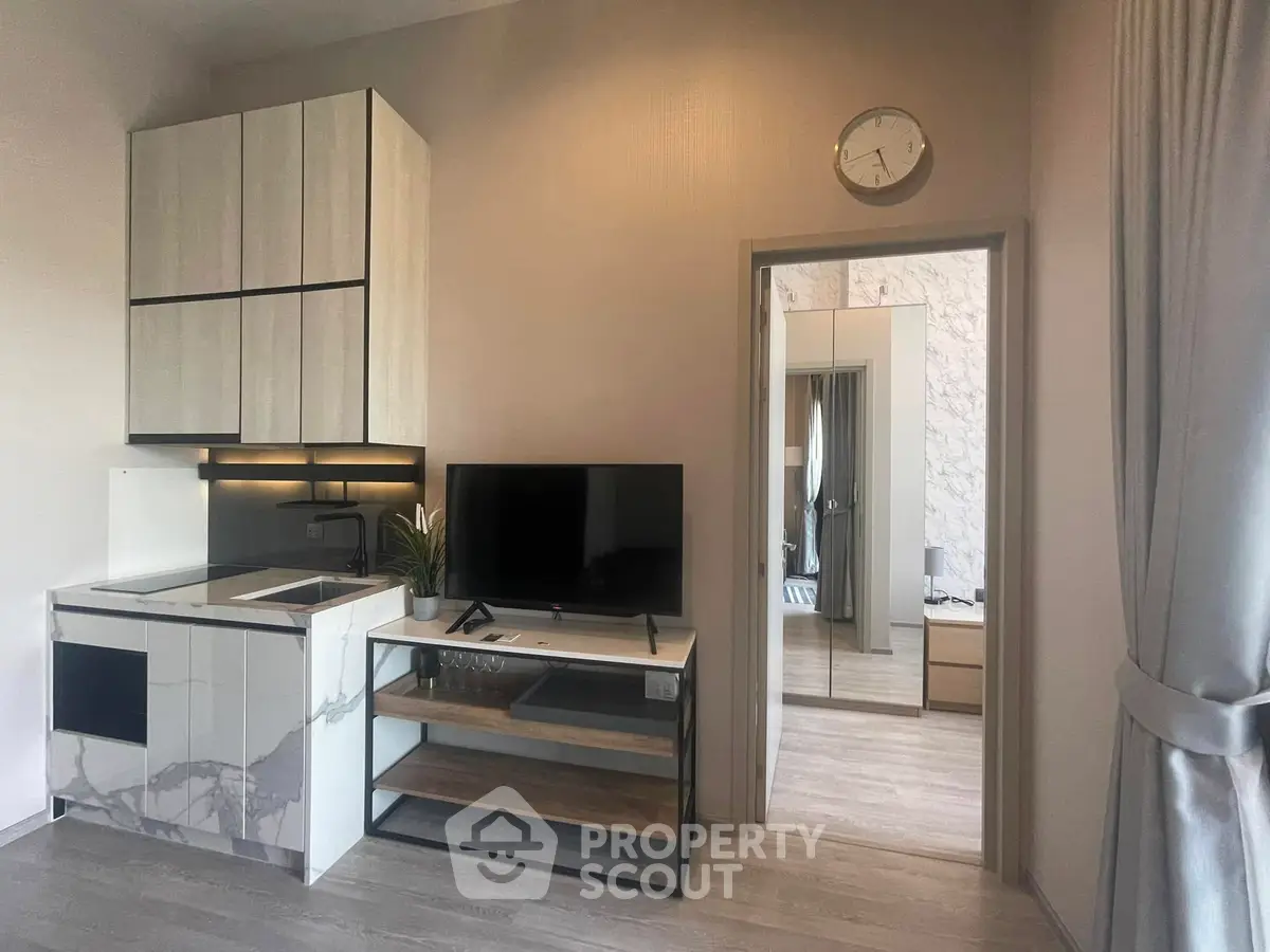 Modern compact living space with sleek kitchen and TV area, featuring stylish decor and natural light.