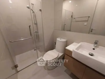 Modern bathroom with glass shower, sleek sink, and toilet in a stylish apartment.