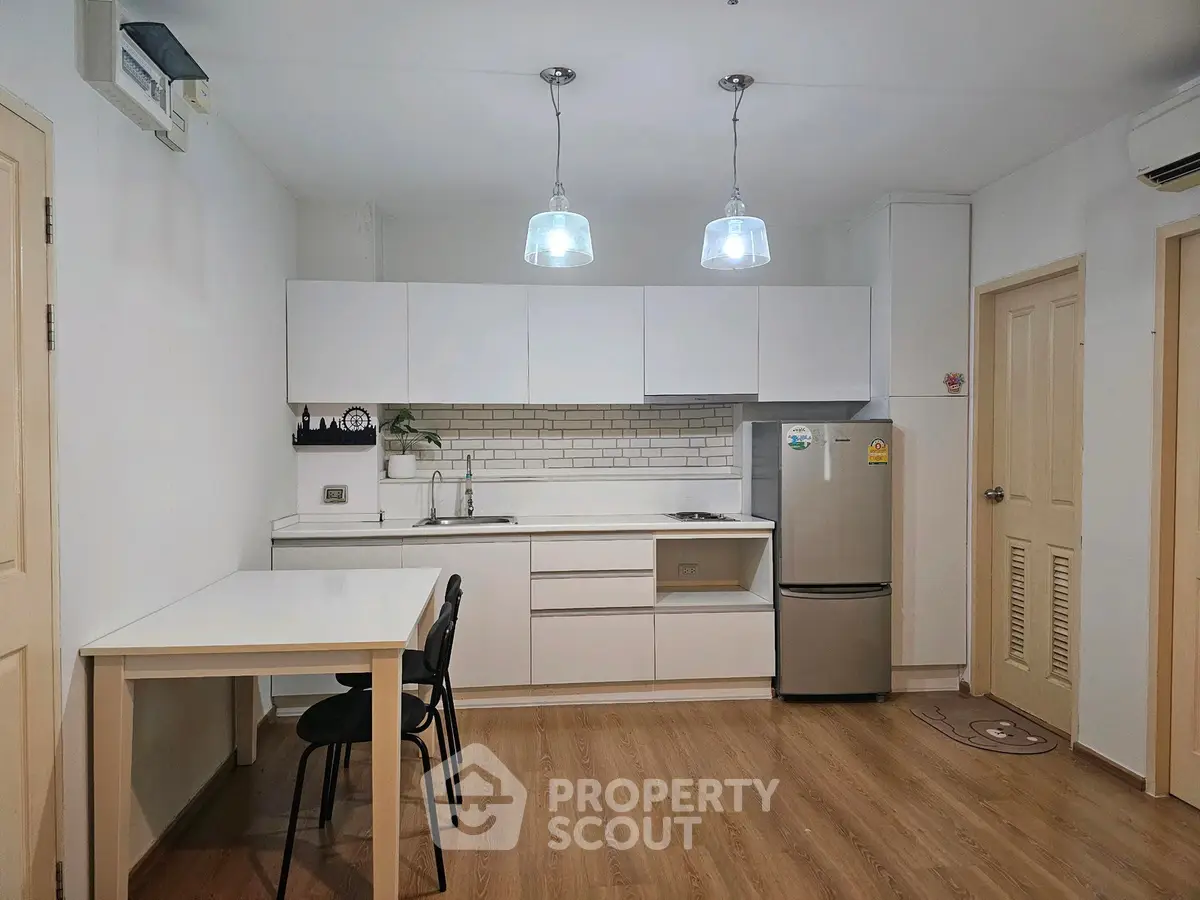 Modern kitchen with sleek white cabinets and stainless steel fridge in a cozy apartment.