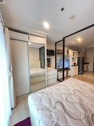 Modern studio apartment with open layout, featuring a cozy bed, mirrored wardrobe, and sleek kitchen area.