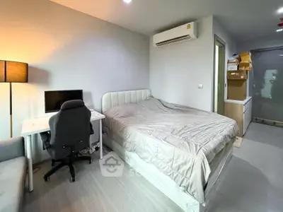 Modern bedroom with workspace, featuring a cozy bed, desk, and chair under soft lighting.