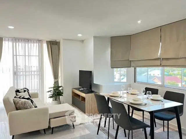 Modern living room with dining area, featuring sleek furniture and large windows for natural light.