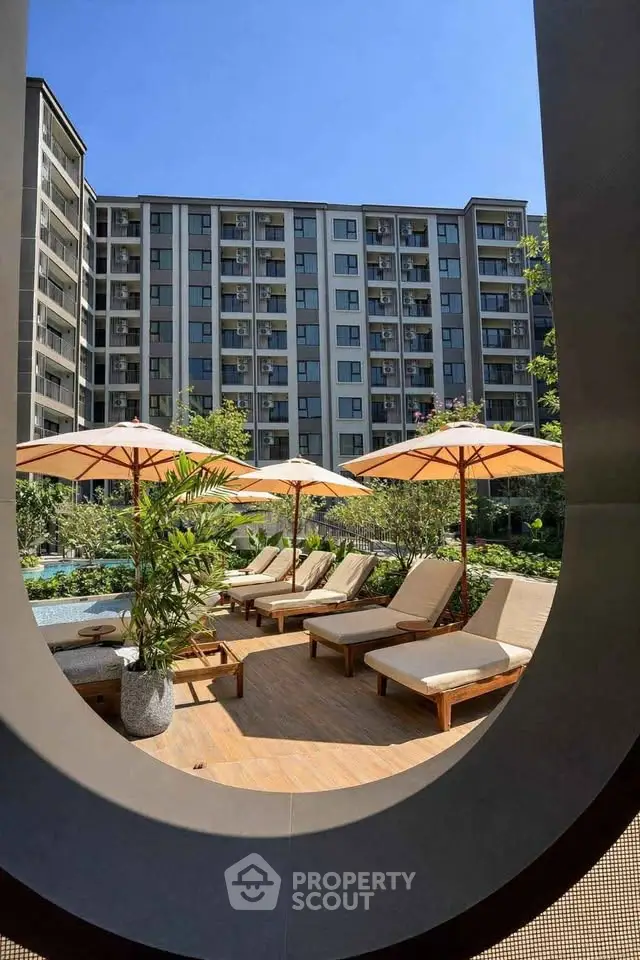 Luxurious apartment complex with poolside lounge chairs and umbrellas, perfect for relaxation.