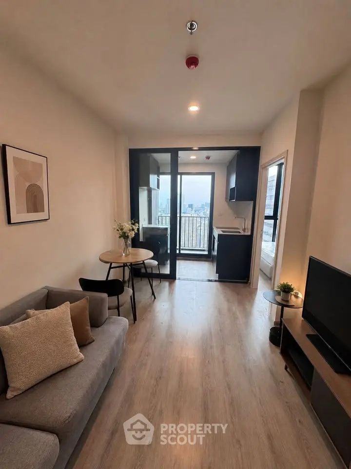 Modern living room with open kitchen and city view, featuring stylish decor and natural light.