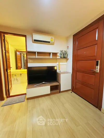 Cozy living room with modern TV setup and wooden flooring, adjacent to a bathroom.