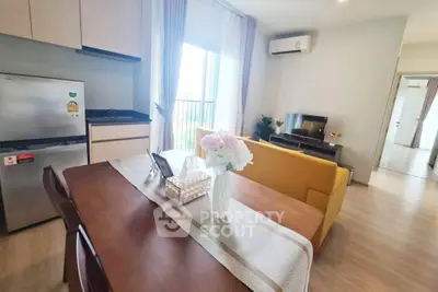 Modern living room with dining area, featuring a cozy yellow sofa, sleek kitchen, and natural light from large windows.