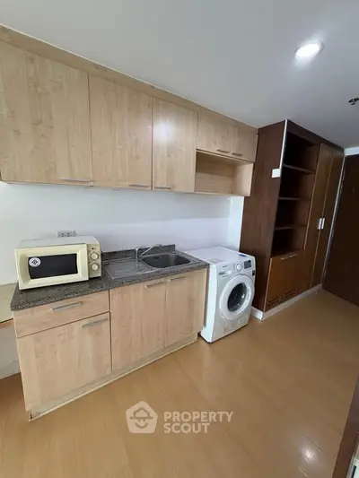 Modern kitchen with wooden cabinets, microwave, and washing machine in a compact layout.