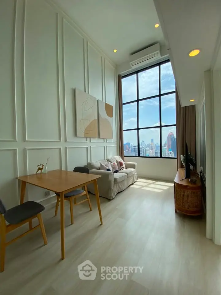 Spacious living room with high ceilings and city view, featuring modern decor and large windows.