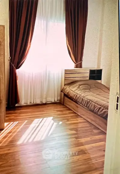 Cozy bedroom with wooden flooring and natural light through large window.