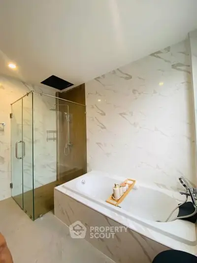 Luxurious bathroom with marble walls, glass shower, and elegant bathtub.