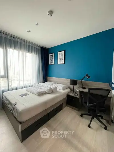 Modern bedroom with blue accent wall, large window, and stylish furniture in a cozy apartment.