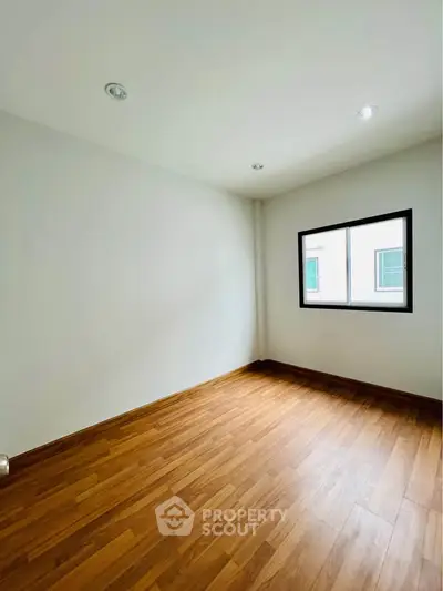 Spacious empty room with wooden flooring and bright window, perfect for customization.