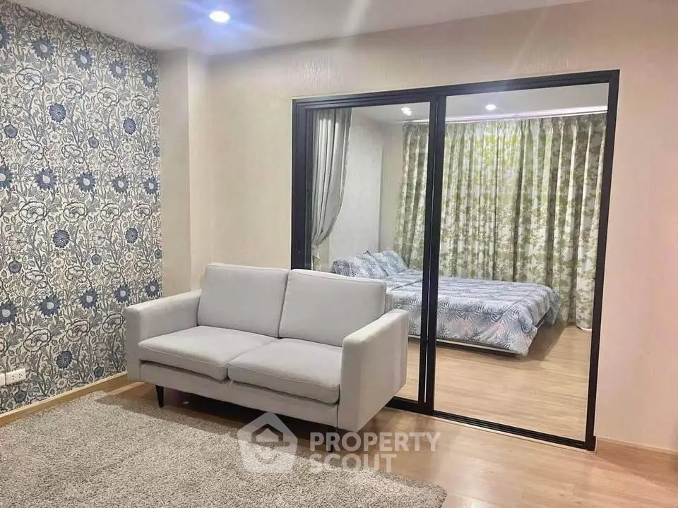 Modern living room with stylish wallpaper and view into cozy bedroom through glass doors.