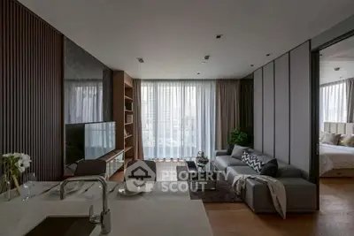 Modern open-plan living room with sleek kitchen and cozy bedroom view, featuring elegant decor and natural light.