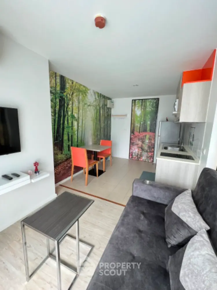 Modern living room with forest-themed wall, sleek furniture, and compact kitchen area.