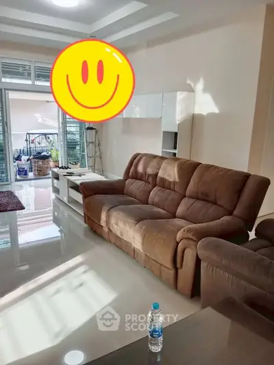 Spacious living room with plush brown sofa and large windows leading to balcony.