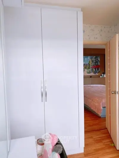 Cozy bedroom with white wardrobe and wooden flooring, offering a glimpse into a well-lit, inviting space.