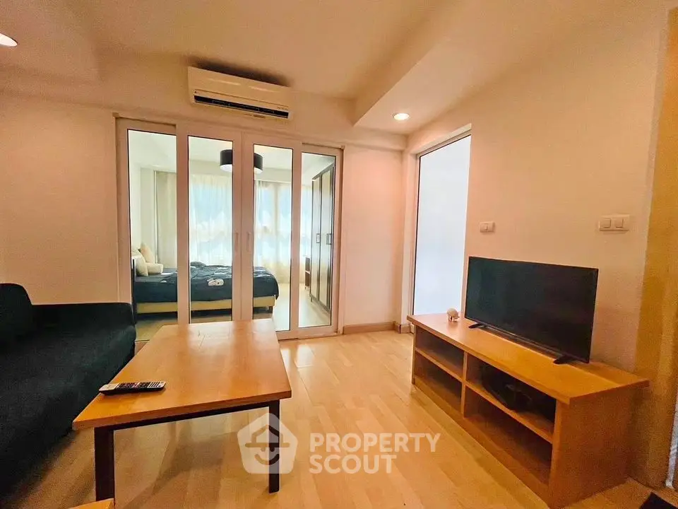 Modern living room with wooden flooring and sliding glass doors leading to a cozy bedroom.