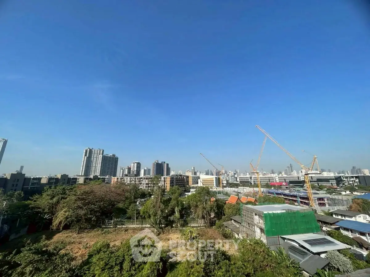 Panoramic cityscape view with construction cranes and urban skyline under clear blue sky.