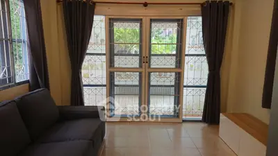 Spacious living room with large windows and garden view, featuring a cozy sofa and elegant curtains.