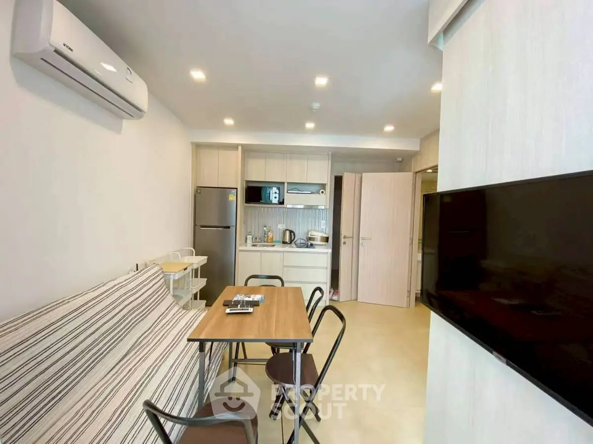 Modern open-plan living room with compact kitchen and dining area, featuring sleek furniture and contemporary design.