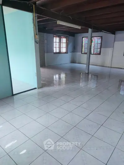 Spacious open-plan room with tiled flooring and wooden ceiling beams.