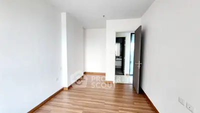 Spacious empty room with wooden flooring and open door leading to bathroom.