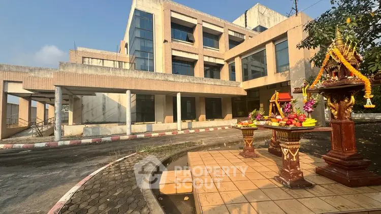 Modern building exterior with traditional decorative shrine in foreground, showcasing unique cultural blend.