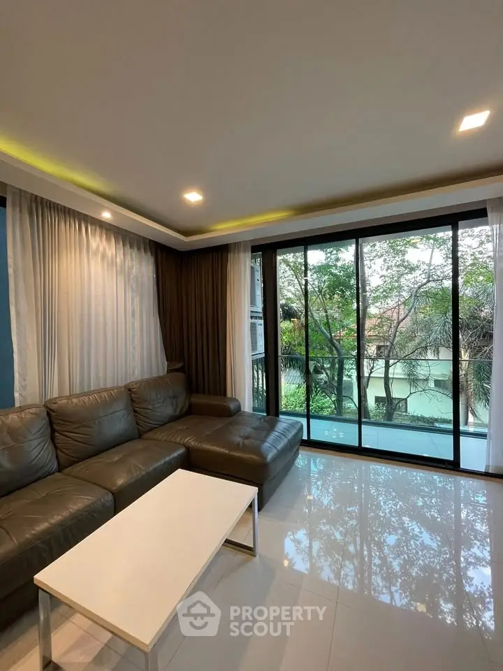 Spacious living room with large windows offering a serene garden view, perfect for relaxation.
