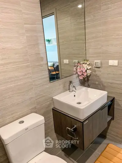 Modern bathroom with sleek sink and toilet, featuring elegant wall tiles and a touch of floral decor.