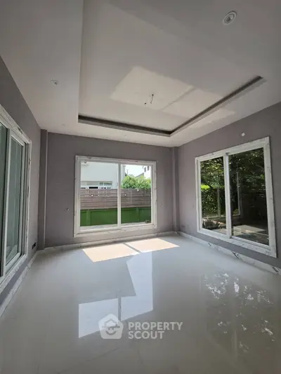 Spacious sunlit room with large windows and glossy white flooring, perfect for modern living.