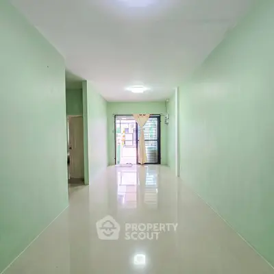 Spacious minimalist living room with glossy floors and pastel green walls, perfect for modern living.